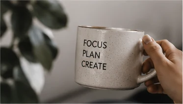 Hand holding a ceramic mug with a simple focus, plan and create message