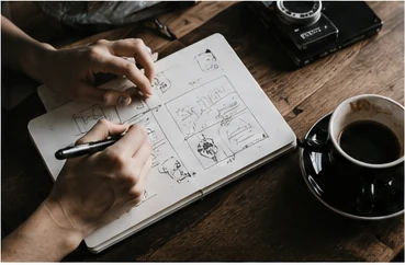 Hands sketching interface ideas and creative concepts in a notebook